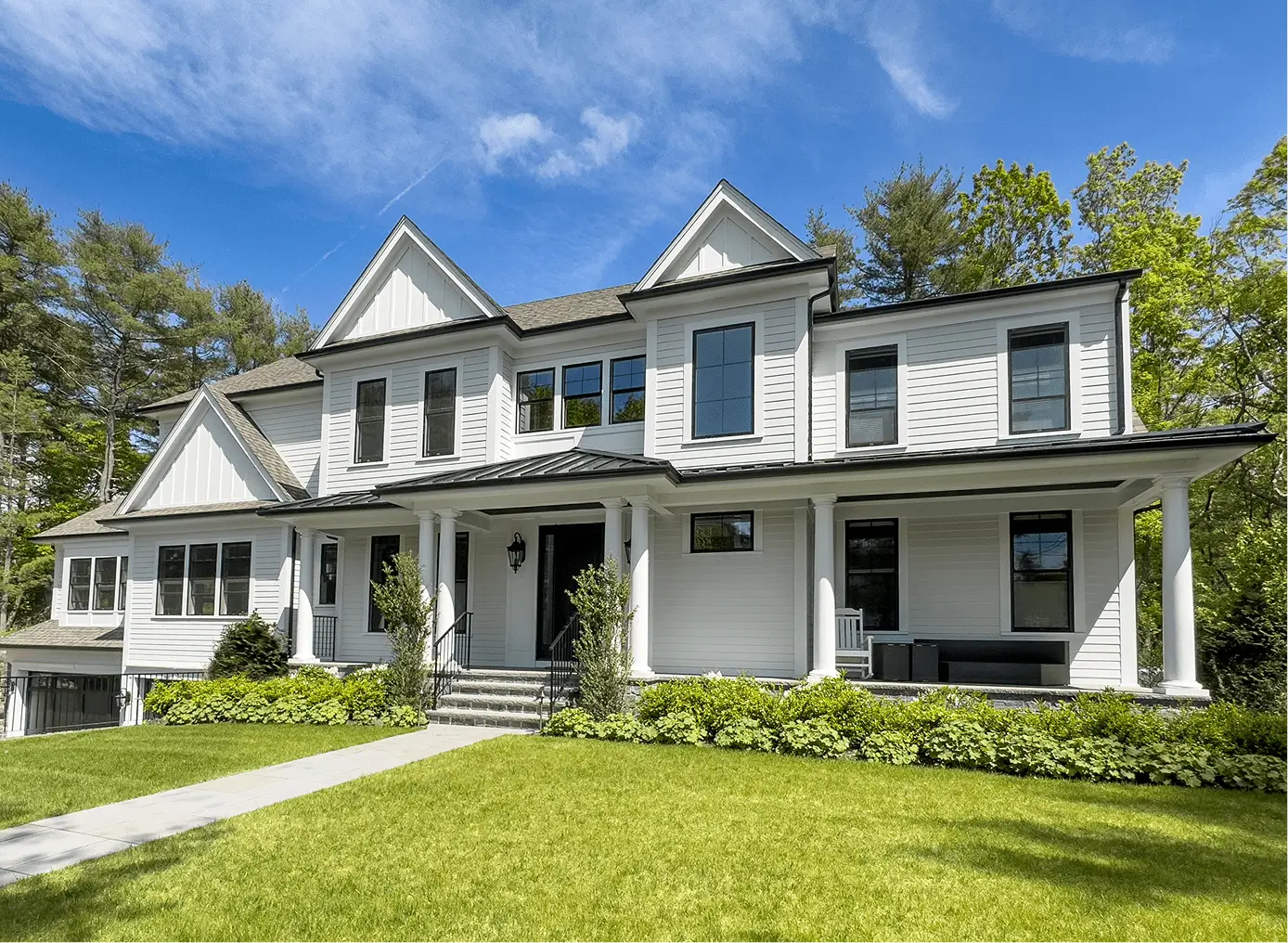 A large two-story white house with a black roof, front porch, and manicured lawn under a clear blue sky. A large two-story white house with a black roof, front porch, and manicured lawn under a clear blue sky.